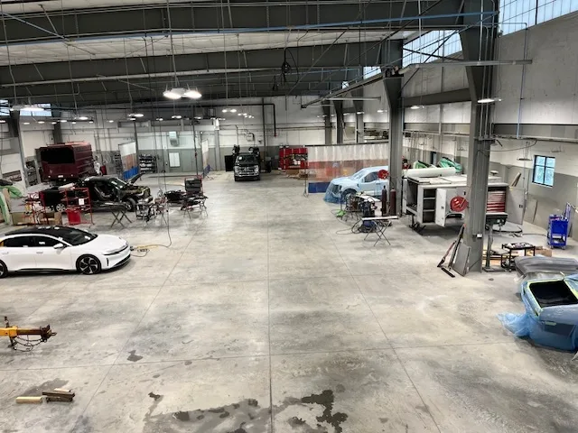 Heritage collision repair bay overview with a Lucid Air, work tables, and multiple vehicles in process, full facility visible