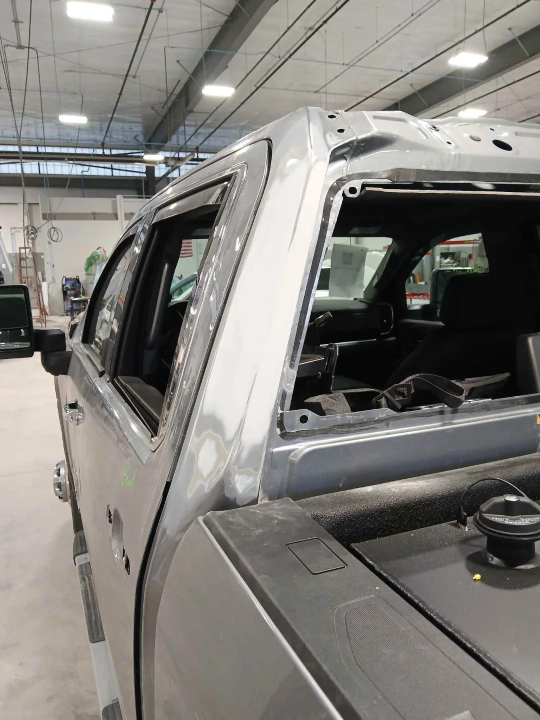 GMC Sierra cab during repair with the rear window removed and the B-pillar exposed, mid-process structural and panel work