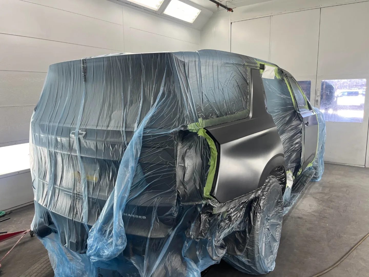 Dark blue Chevy Tahoe Supercharged masked in the spray booth with primer-coat rear quarter panel visible, mid-repair