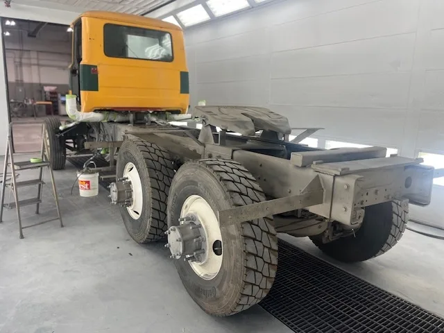 Yellow commercial truck cab and chassis from the rear inside the spray booth, ready for refinish work
