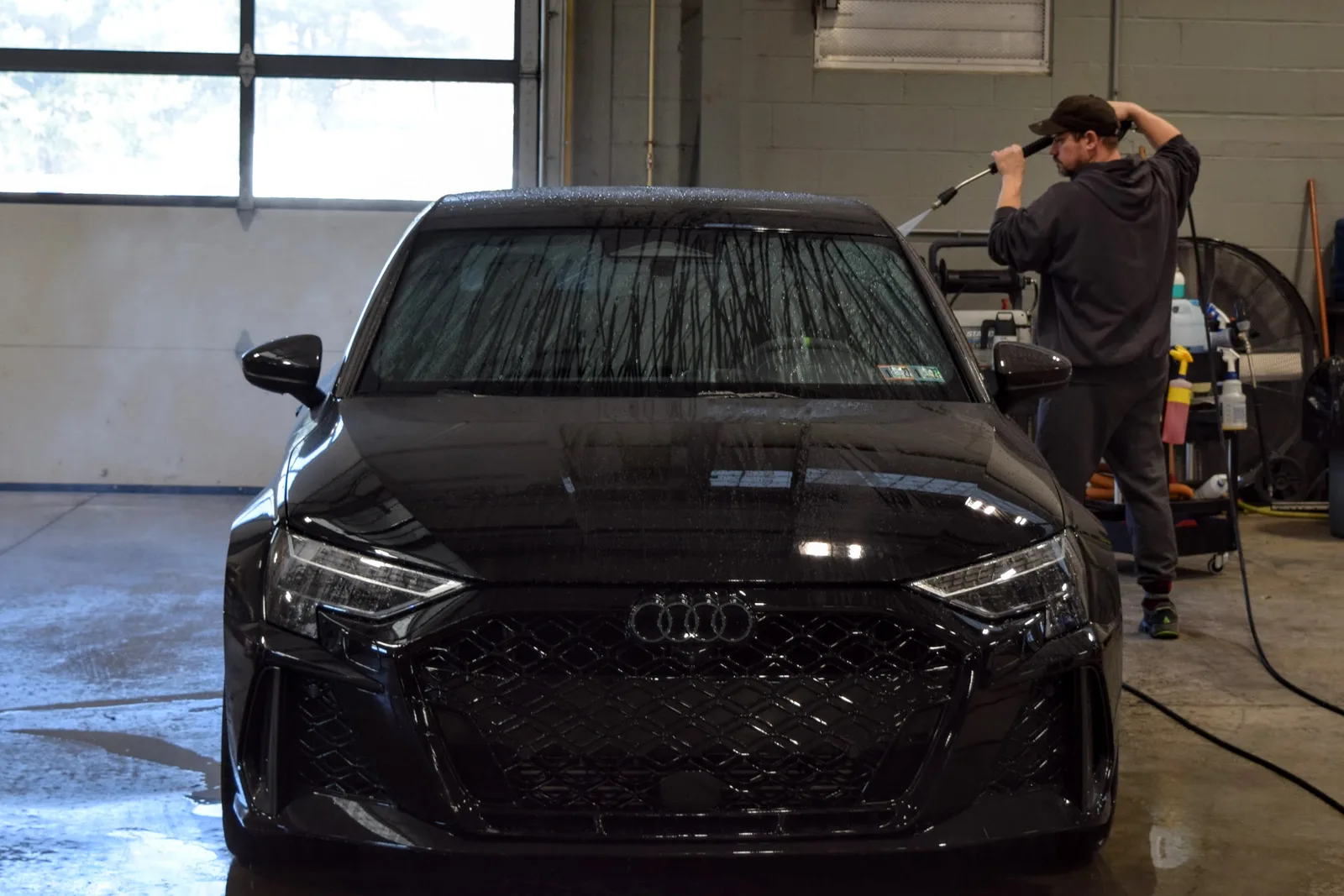 Heritage technician pressure washing the windshield of a black Audi RS3 during decontamination wash