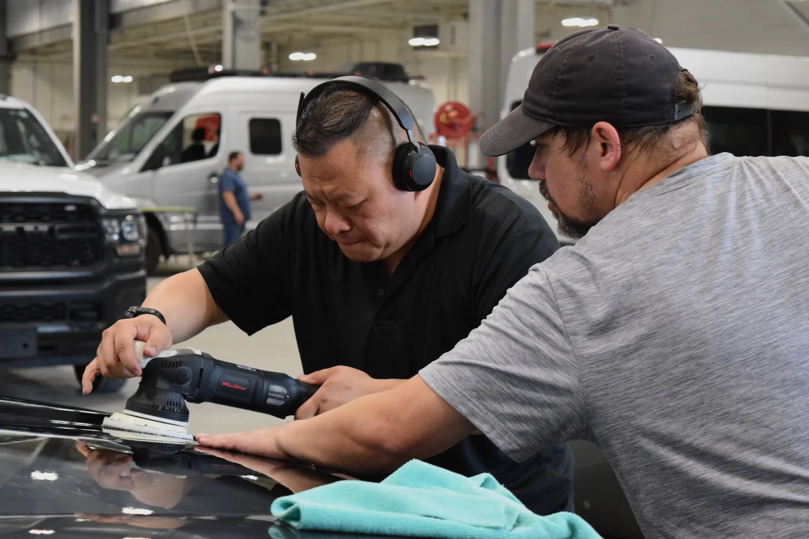 Two Heritage technicians machine polishing a black hood together with a dual-action orbital polisher