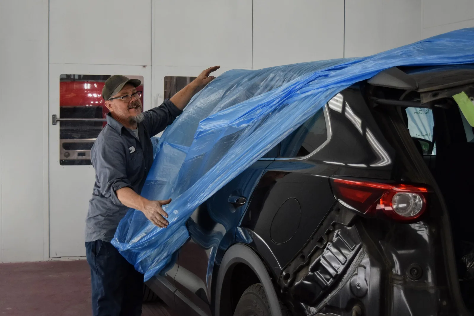 Heritage technician masking a vehicle with blue plastic sheeting in the booth before PeelClear spray application