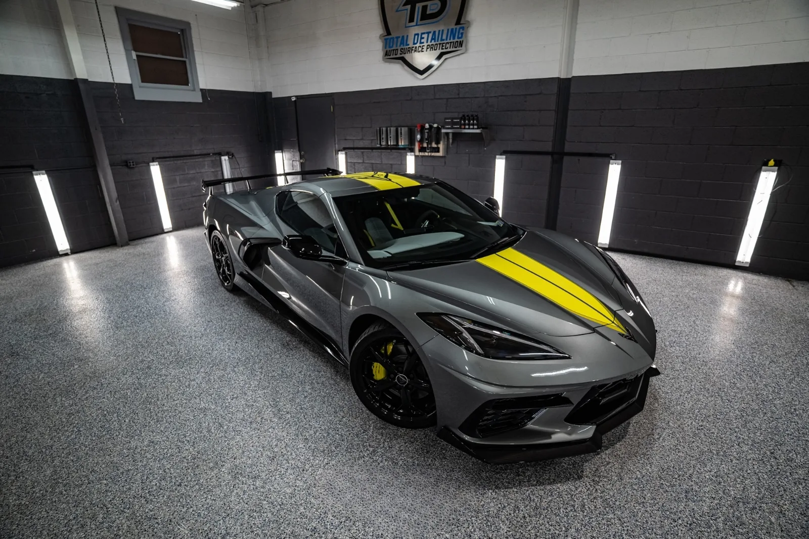 Hypersonic Gray Chevrolet Corvette C8 with yellow racing stripe, front three-quarter in shop bay