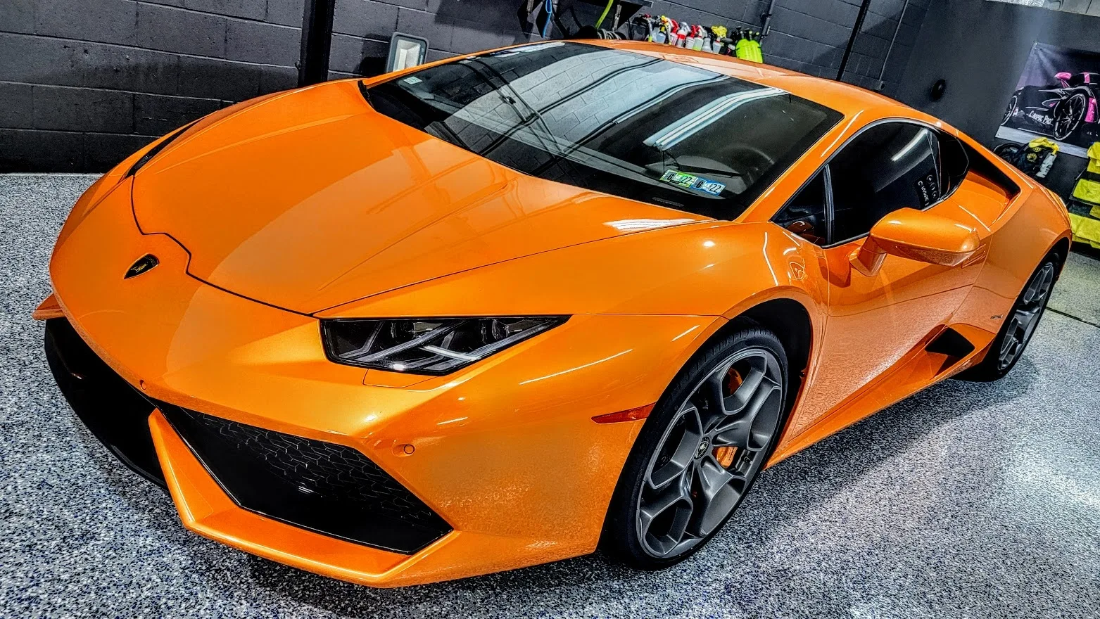 Orange Lamborghini Huracán front three-quarter view in shop bay, deep gloss paint finish