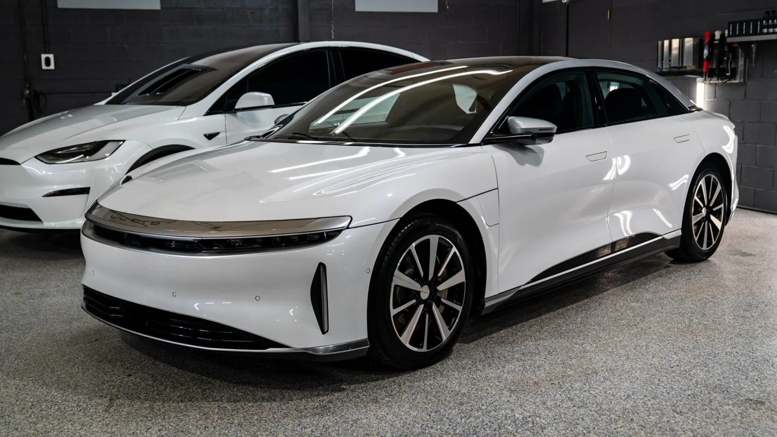 White Lucid Air sedan with Tesla Model Y behind it in the Heritage shop bay, both freshly detailed