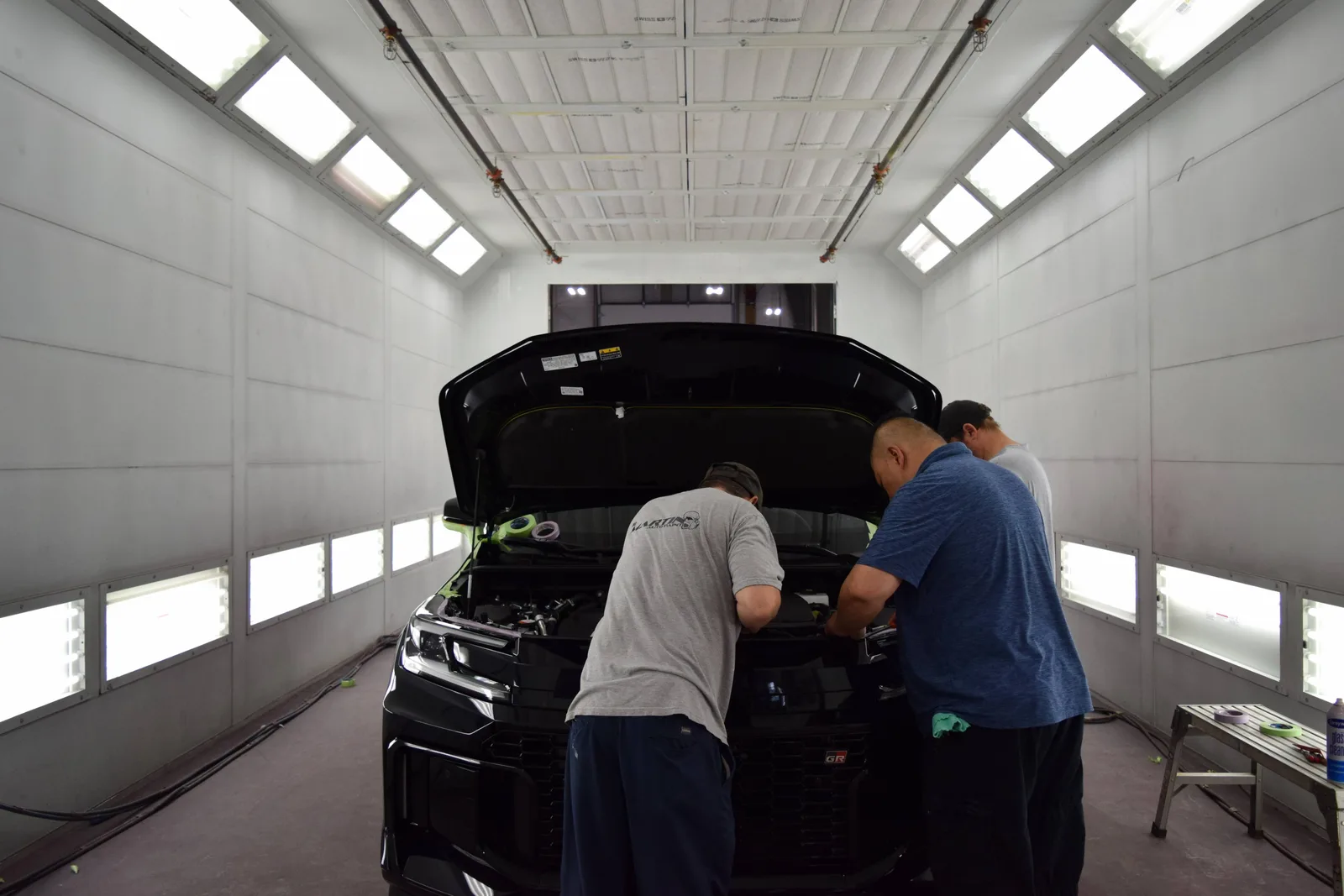 Two Heritage technicians prepping a black SUV under the hood in the spray booth before PeelClear