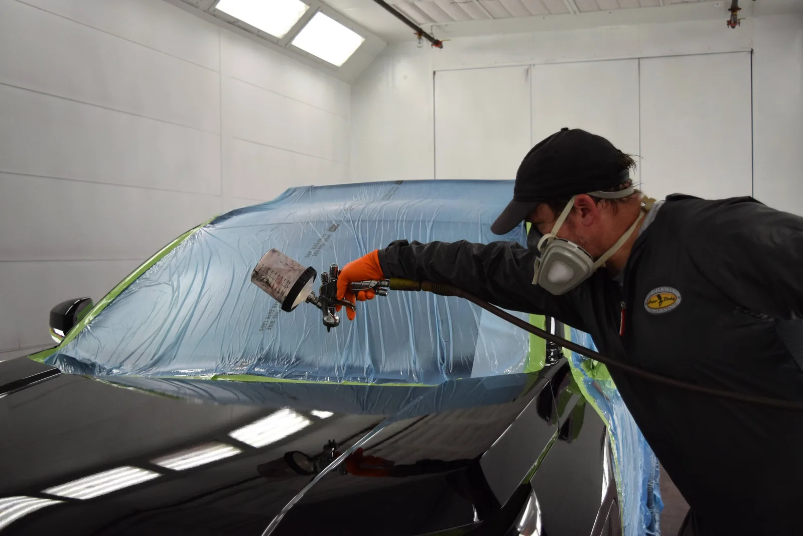 Heritage technician spraying PeelClear topcoat in the booth wearing respirator and orange nitrile gloves