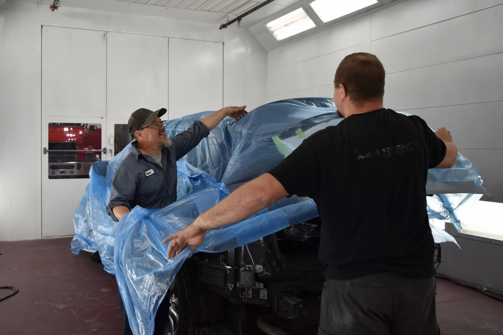 Two Heritage technicians removing blue masking film from a freshly sprayed vehicle in the paint booth