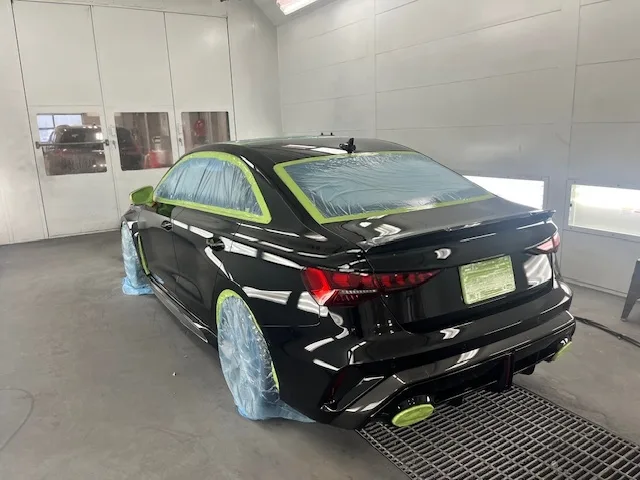 Black Audi RS3 sedan in paint booth, rear three-quarter view, masked for PeelClear application