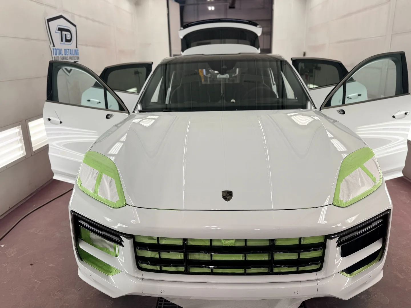White 2026 Porsche Cayenne in paint booth with grille and headlights masked, ready for full-body PeelClear